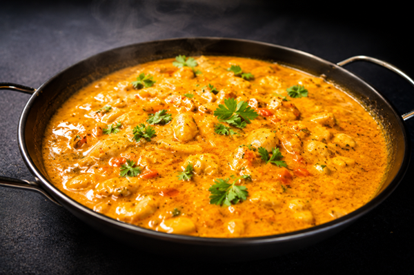 Arroz meloso de langosta y coco servido caliente en una paellera metálica de dos asas, decorado con trozos de mariscos y hojas frescas de cilantro.