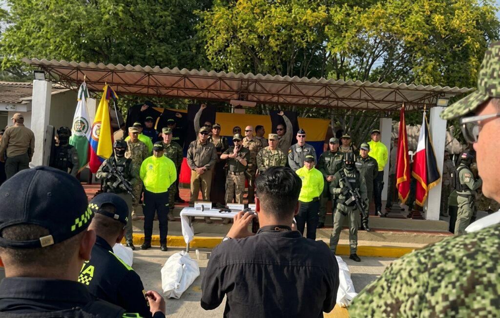 Fotografía de una Rueda de Prensa de la Fuerza Pública en Riohacha, La Guajira. En el centro de la tarima, autoridades militares y de la Policía Nacional acompañan al Presidente durante sus declaraciones institucionales tras el operativo contra alias 'El Bendito Menor'. Al frente se observan periodistas registrando el evento y elementos incautados sobre una mesa.
